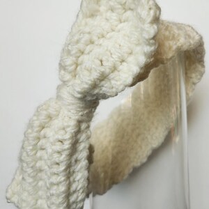 May include: A white crocheted headband with a large bow. The headband is made with a soft, chunky yarn.