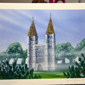 May include: A watercolor painting on paper depicting a stone church with two tall towers featuring pointed golden roofs. The structure is surrounded by green trees and foliage under a light blue sky. The artist's signature is visible in the corner.