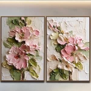 May include: A diptych wall art set featuring two rectangular canvases with thick, textured impasto oil paint. The artwork displays large, layered pink flowers with sage green leaves against a cream-colored background, framed in thin wood.