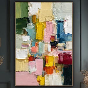 May include: Abstract oil painting with a gold frame. The artwork features a textured, colorful composition of rectangular shapes in shades of pink, yellow, blue, green, and white. The painting is displayed on a dark gray wall.
