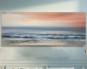 May include: Abstract painting of a seascape with a soft pink and orange sunset over a blue ocean with white waves crashing on the shore. The painting is framed in a thin gold frame and is hanging on a light blue wall above a white couch.