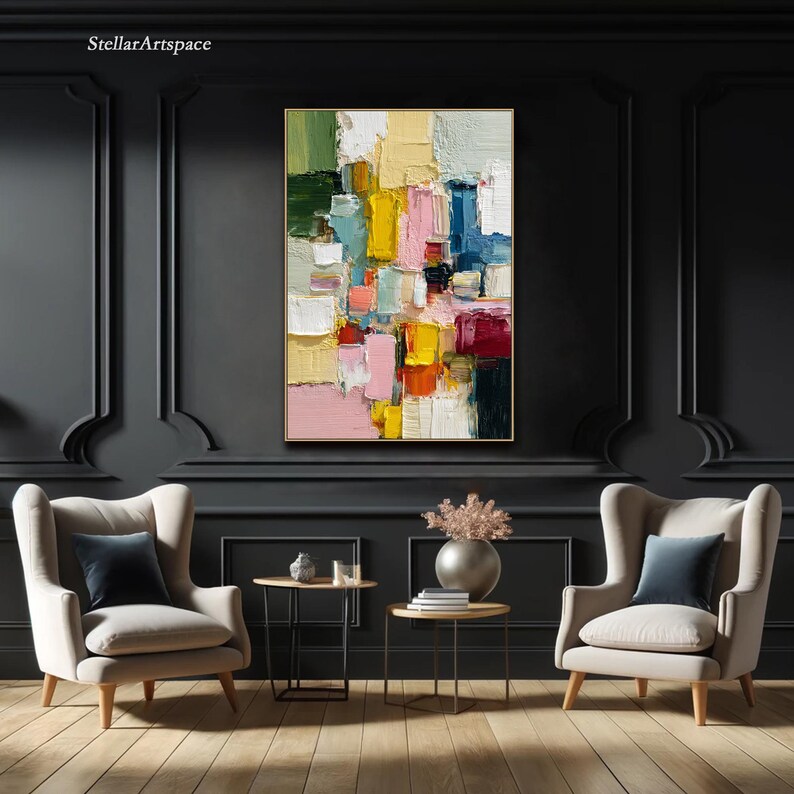May include: Abstract oil painting with a gold frame. The artwork features a colorful composition of rectangular shapes in shades of yellow, pink, blue, green, and red. The painting hangs on a dark gray wall above two armchairs.