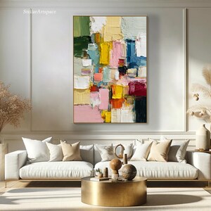 May include: Abstract oil painting with a gold frame. The artwork features a colorful composition of rectangular shapes in shades of green, yellow, pink, blue, and red. The painting is displayed above a white sofa with decorative pillows.