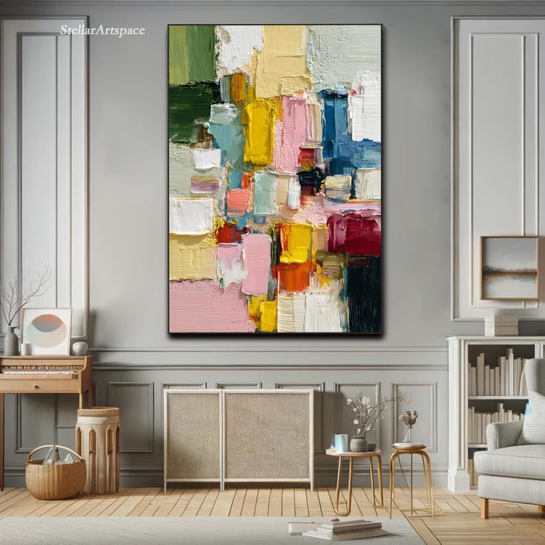 May include: Abstract oil painting on canvas with a black frame. The artwork features a vibrant mix of colors, including pink, yellow, blue, and green, applied in thick brushstrokes. The painting has a textured appearance and is displayed in a well-lit room.