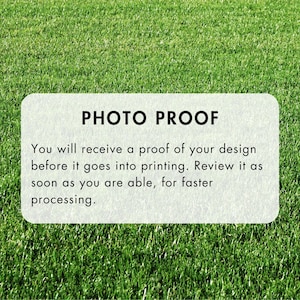 May include: A rectangular, off-white sign with rounded corners, set against a backdrop of green grass. The sign reads "PHOTO PROOF" in bold, black letters. Below, smaller text explains the proofing process before printing.