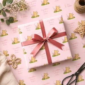 May include: A square gift box wrapped in light pink paper featuring a repeating pattern of Winnie the Pooh and Piglet illustrations, with the text Congratulations Amelia & Andrew and Love, love, the Walkers, tied with a dusty rose satin ribbon.