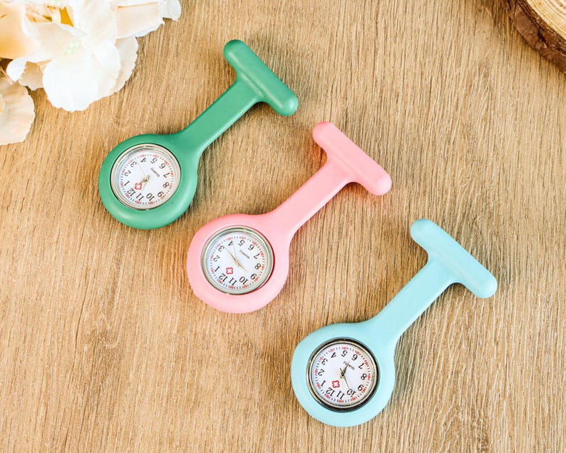 May include: Three colorful fob watches in green, pink, and light blue. Each watch has a white clock face with black numbers and red hands. The watches are designed with a T-shaped top for easy attachment.