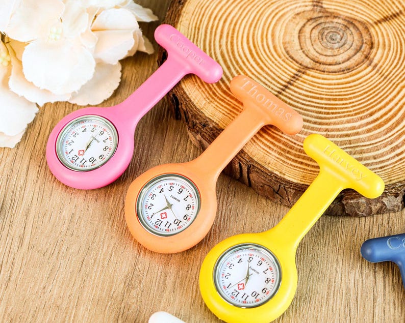 May include: Three colorful fob watches in pink, orange, and yellow. Each watch has a white face with black numerals and hands. The pink watch has "Cooper" printed on the handle, the orange watch has "Thomas", and the yellow watch has "Harvey".