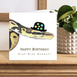 May include: A birthday card featuring a snake wearing a black and white polka dot hat. The card reads "Happy Birthday, Hiss Hiss Hooray!"