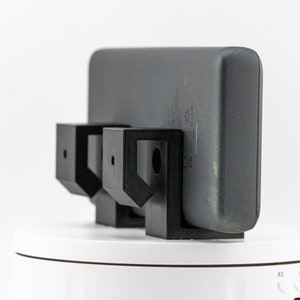 May include: A black phone charger stand with two black brackets holding a gray phone charger.