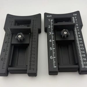 May include: Two black adjustable alignment tools featuring white printed markings. Each tool includes a sliding component with a central black knob, a scale measuring up to 6 inches on the left, and a scale measuring up to 18 cm on the right.