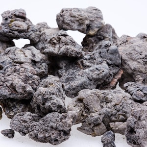 May include: A close-up of a pile of dark gray volcanic rocks. The rocks are rough and textured, with a variety of shapes and sizes.