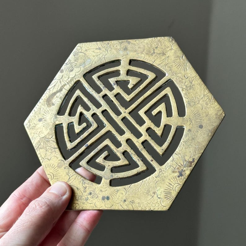 May include: A hexagonal brass ornament with a decorative, intricate, geometric design in the center. The ornament is engraved with floral patterns around the edges.