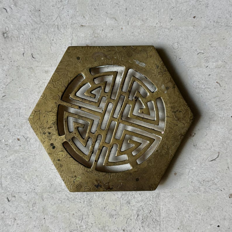 May include: A hexagonal brass coaster with a decorative, cut-out design in the center. The design is a circular pattern of interlocking squares.