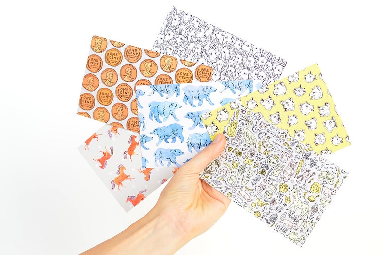 May include: Six different patterned sheets of paper. The patterns include a repeating image of a penny, a bear, a cat, a unicorn, a horse, and a variety of small drawings.