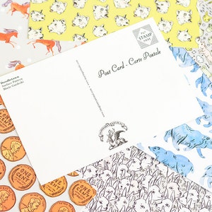 May include: A set of four different patterned postcards with a blank postcard on top. The patterns include a repeating image of a penny, a repeating image of a dog's face, a repeating image of a blue bear, and a repeating image of a cat's face. The blank postcard has the text "Post Card - Carte Postale" printed on it.