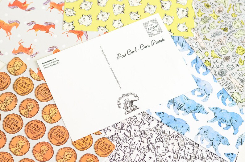 May include: A set of four different patterned postcards with a blank postcard on top. The patterns include a repeating image of a penny, a repeating image of a dog's face, a repeating image of a blue bear, and a repeating image of a cat's face. The blank postcard has the text "Post Card - Carte Postale" printed on it.