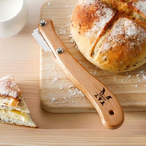 May include: A wooden bread lame with a personalized inscription "Mary + IV" on the handle. The lame has a serrated blade and is used for scoring bread before baking.