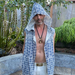 Puede incluir: Un chaleco sin mangas con capucha con un patrón geométrico azul y blanco. El chaleco está abierto en la parte delantera y tiene un diseño largo y fluido. La persona que lleva el chaleco también lleva pantalones blancos y un collar con un colgante.