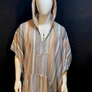 May include: A hooded poncho featuring a vertical striped pattern in shades of brown, gray, white, and tan. The garment has a V-neckline, short sleeves, and a front kangaroo pocket. A gold-toned necklace with a pendant is worn around the neck.