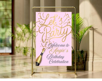 May include: A pink sign with gold lettering that reads "Let's Party" and "Welcome to Angie's Birthday Celebration." A gold champagne bottle graphic is included. The sign is held by a gold metal frame.