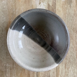 May include: A white ceramic bowl with a black and grey glaze. The bowl is divided in half, with one side being white and the other side being black and grey.