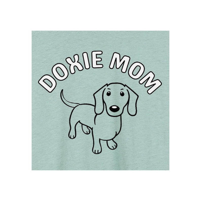 May include: A light blue t-shirt with the text "DOXIE MOM" in white letters with a black outline. A cartoon dachshund is centered below the text.