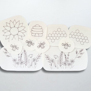May include: A black and white illustration of a beehive, honeycomb, sunflower, and bees. The illustration is on a white background.