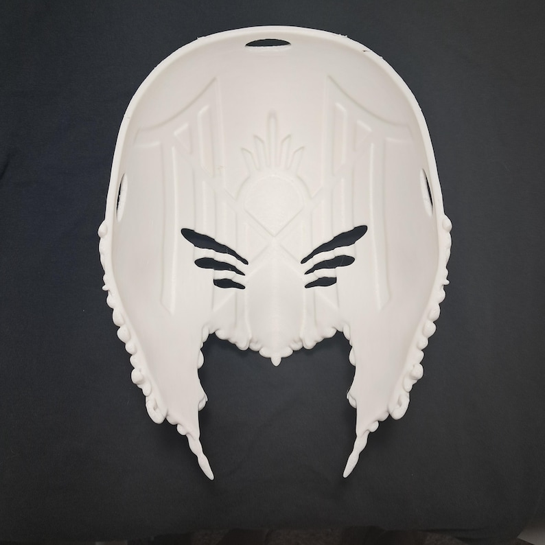 May include: White plastic mask with intricate details and a pointed chin. The mask has a design of a stylized face with a crown on top.