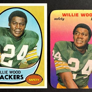 May include: Two vintage football trading cards featuring Willie Wood of the Green Bay Packers. The cards show Wood in his green and gold uniform with the number 24. One card has a yellow background, the other a pink and purple background.