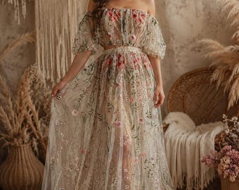 May include: A two-piece set consisting of an off-the-shoulder crop top with puff sleeves and a matching floor-length skirt. Both pieces are made of sheer, light-colored fabric featuring intricate, multi-colored floral embroidery throughout.