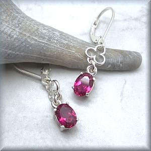 May include: A pair of silver earrings with a pink oval gemstone and a clover charm.