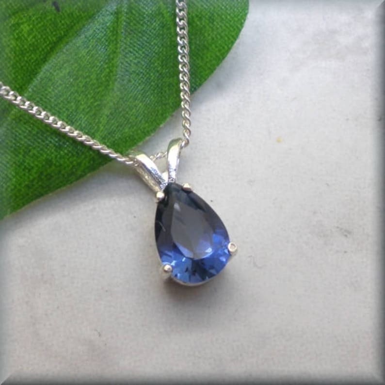 Pode incluir: Um colar de corrente de prata com um pingente de pedra preciosa azul em forma de p&ecirc;ra.