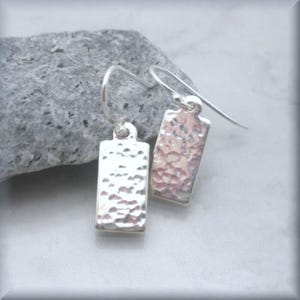 May include: A pair of silver earrings with a hammered texture. The earrings are rectangular in shape and have a simple hook closure.