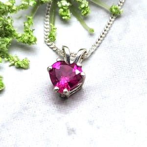 May include: A silver chain necklace with a heart-shaped pendant featuring a pink gemstone.