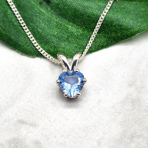 May include: A silver chain necklace with a heart-shaped pendant featuring a light blue gemstone.