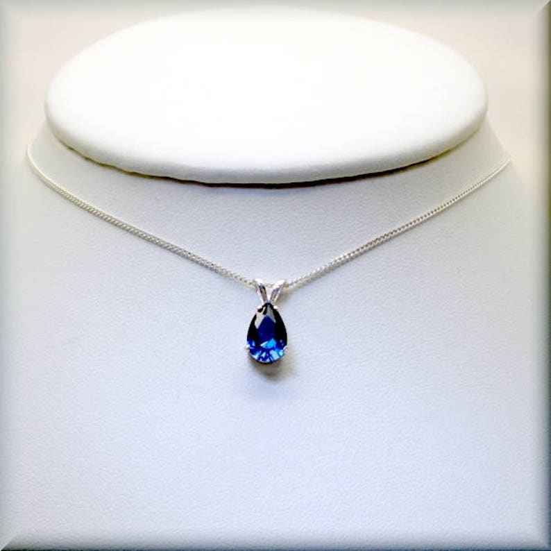 Pode incluir: Um colar de corrente de prata com um pingente de pedra preciosa azul em forma de l&aacute;grima.