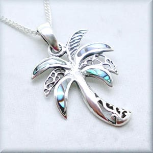 May include: A silver palm tree pendant necklace with abalone shell inlay. The pendant is detailed with a delicate, intricate design.