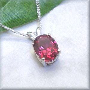 May include: A silver chain necklace with a pendant featuring a large, oval-shaped, bright pink gemstone.