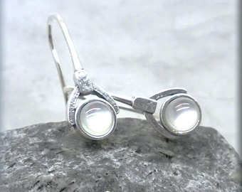 May include: A pair of silver earrings with white pearl-like stones. The earrings have a unique design with a curved shape and a small loop at the top.