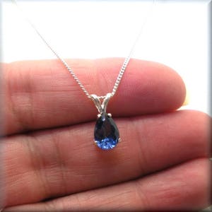 Pode incluir: Um colar de corrente de prata com um pingente de pedra preciosa azul em forma de p&ecirc;ra.