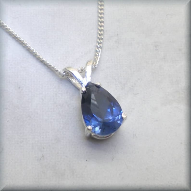 Pode incluir: Um colar de prata com um pingente de pedra azul em forma de p&ecirc;ra.