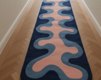 Pode incluir: Um tapete passadeira retangular longo com um fundo azul-marinho escuro e um padrão ondulado contínuo ao centro, em tons de azul-claro e rosa suave. O design consiste em formas orgânicas e fluidas que percorrem todo o comprimento do tapete.