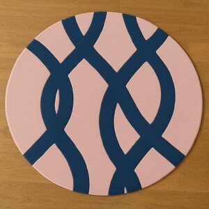 May include: A round rug with a pink background and a navy blue interwoven design. The rug's pattern creates a series of overlapping loops, offering a modern and geometric aesthetic. The rug is suitable for various interior spaces.