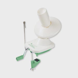 Op de afbeelding: Een wit en lichtgroen garenwinder met een centrale spil, een draaiende schijf, een metalen garengeleider en een slinger. De basis is bedrukt met de tekst "Bee in my Bonnet" in groen schrift, vergezeld van een kleine afbeelding van een bij.