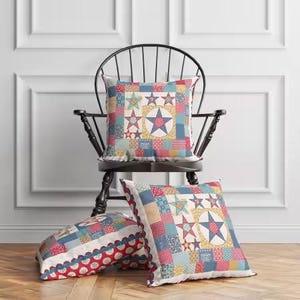 May include: Three decorative throw pillows with a patchwork star design in red, white, blue, and yellow. One pillow rests on a black chair, while the other two are on the floor. The pillows have a quilted appearance.