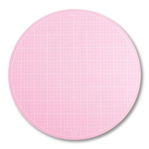 Puede incluir: Una esterilla de corte redonda de color rosa claro con un patrón de cuadrícula. La esterilla tiene una cuadrícula blanca y un borde rosa ligeramente más oscuro. Aproximadamente 30 cm de diámetro, ideal para manualidades.