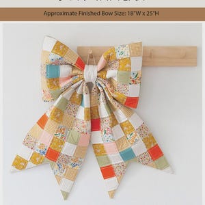 May include: A patchwork quilted bow with a finished size of 45.72 cm wide by 63.5 cm high. The bow features a grid of squares in yellow, orange, teal, pink, and floral patterns. Text reads: PATCHWORK QUILTED BOW PATTERN, Brooklyn Dawn Quilt Co.
