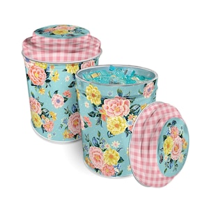 Op de afbeelding: Twee decoratieve metalen containers met deksels. De containers hebben een lichtblauwe achtergrond met een bloemenpatroon in roze, geel en perzik. De deksels en randen hebben een roze en wit geruit patroon.