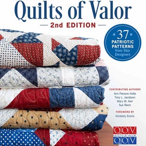May include: A stack of patriotic quilts with red, white, and blue patterns. The book "Quilts of Valor" is visible, with text indicating 37 patriotic patterns from Star Designers. The quilts are folded and stacked on top of each other.